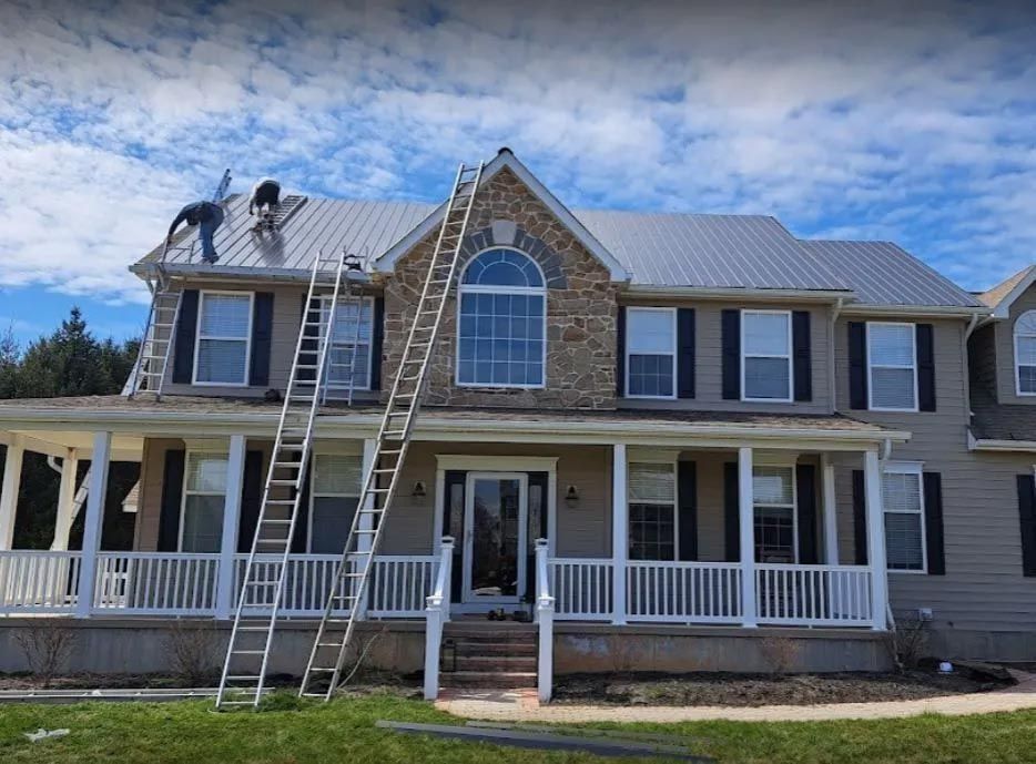 Roofer wearing a yellow hard hat and safety vest uses a drill on a roof in sunlight.