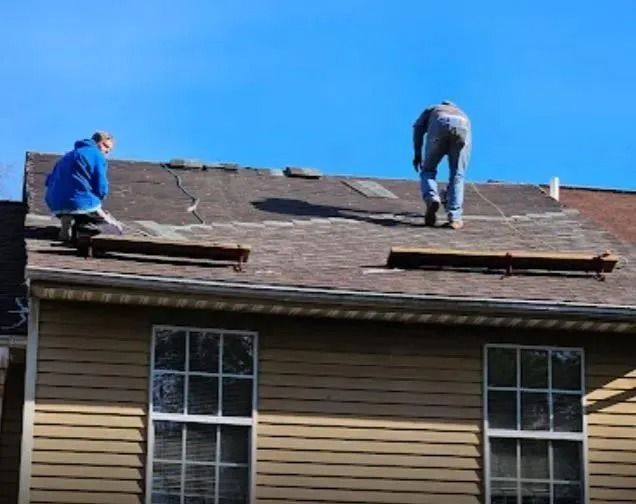 Three workers installing metal roof tiles on a house under construction.