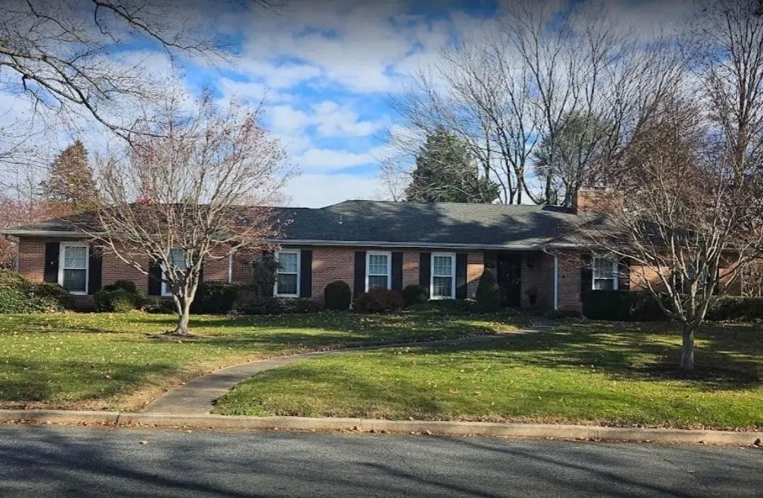 Brick ranch home with a lawn and bare trees against a blue sky.