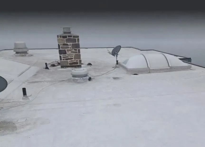 Snow-covered flat rooftop with a stone chimney, vents, and a skylight.