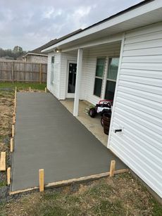 Newly poured concrete patio alongside a white house with wood formwork still in place.