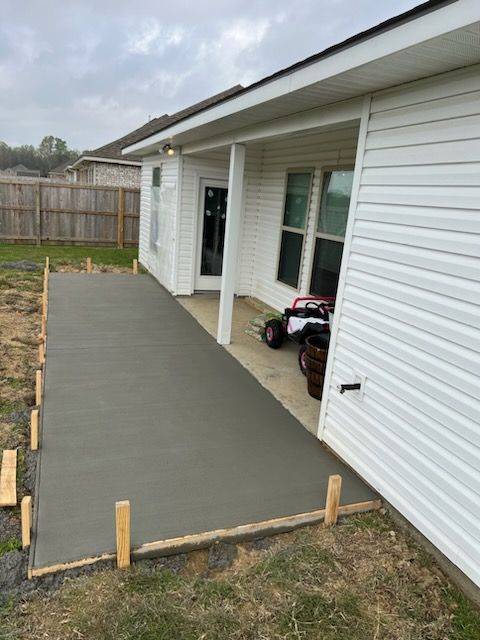 Newly poured gray concrete patio next to a white house with a small child's car and barrels on it.