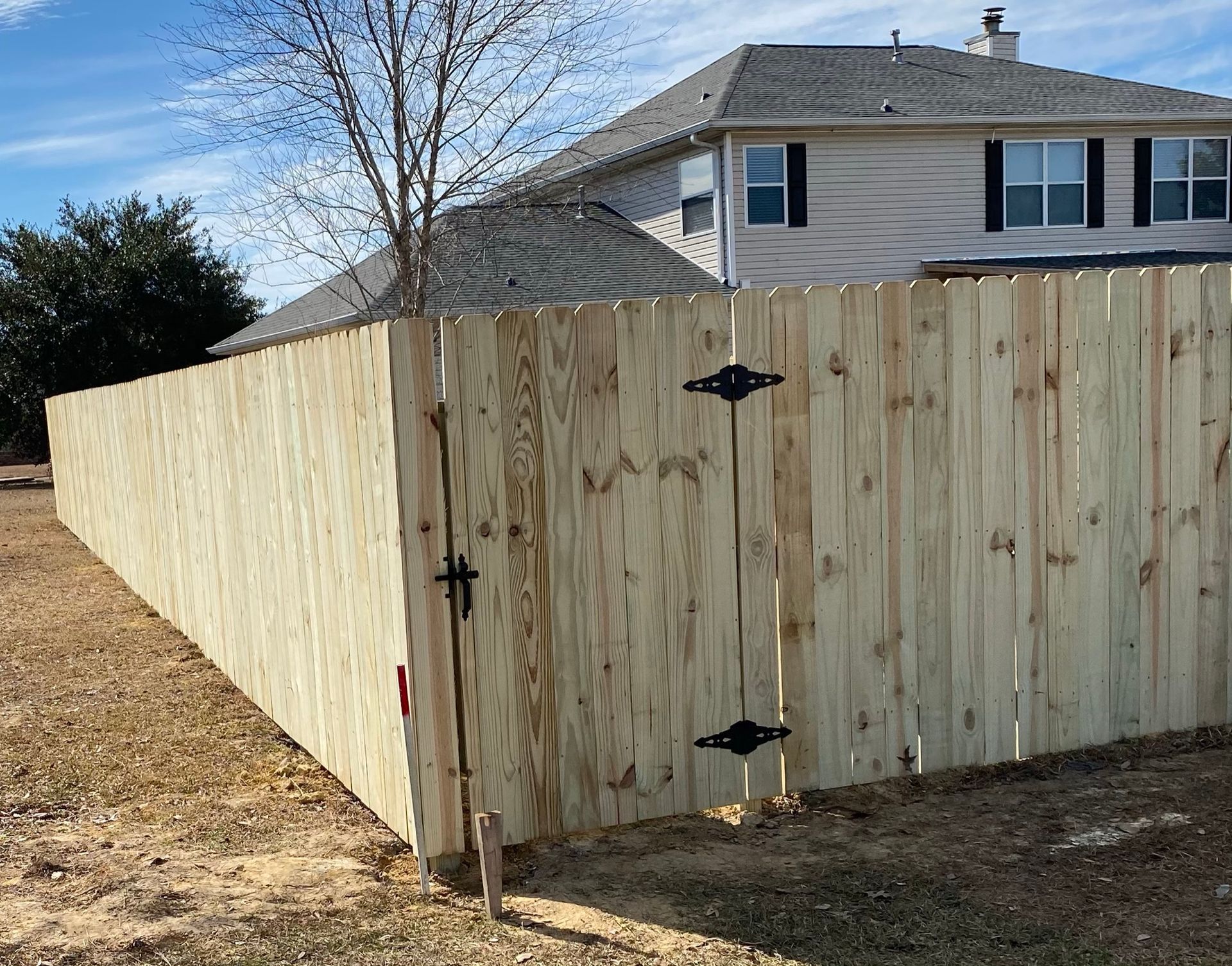 Wooden fence with a gate, surrounding a yard, in front of a two-story house.