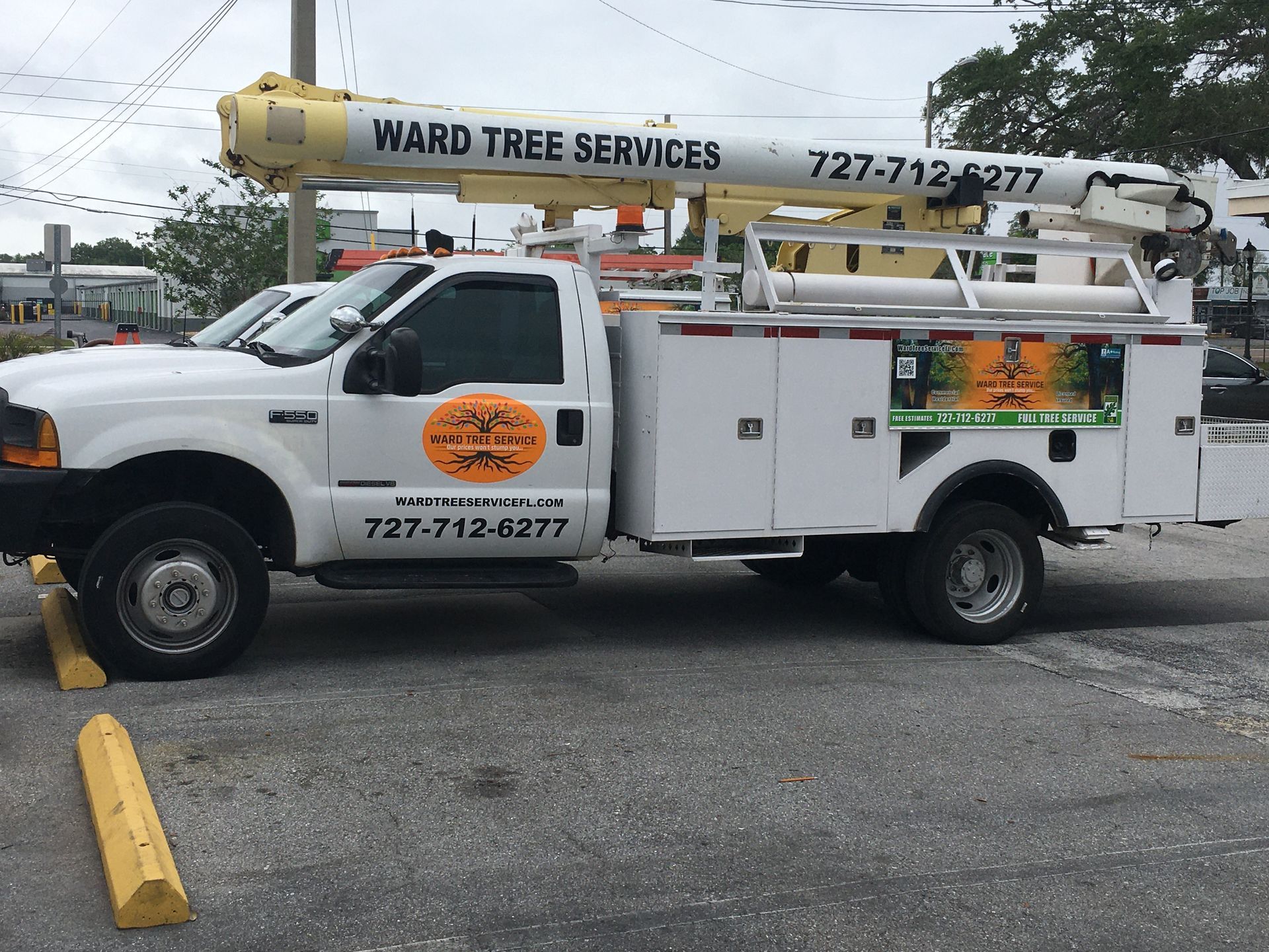 A white Ward Tree Services utility truck with a yellow bucket arm, parked in a parking lot.