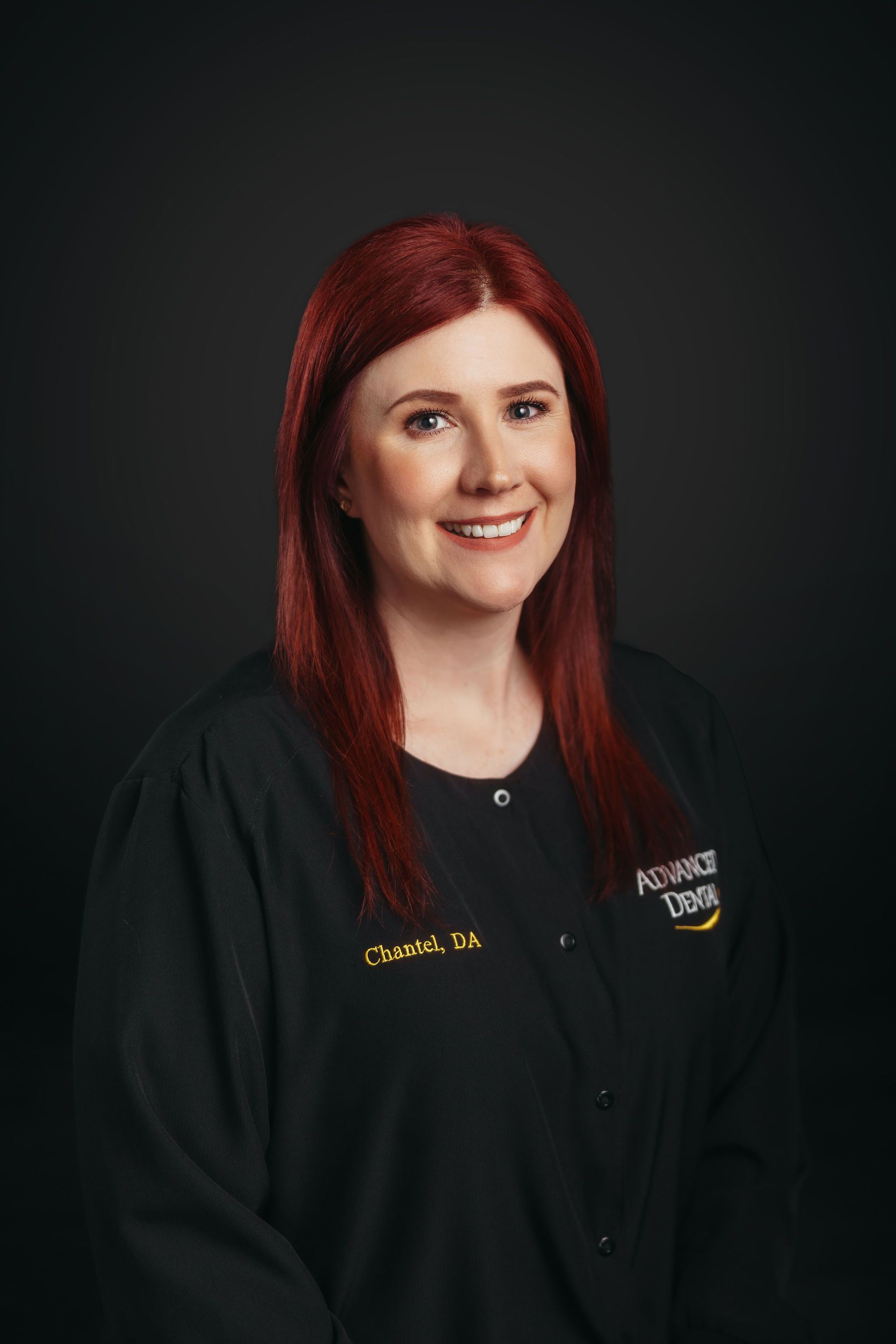 A woman with red hair is wearing a black jacket and smiling.