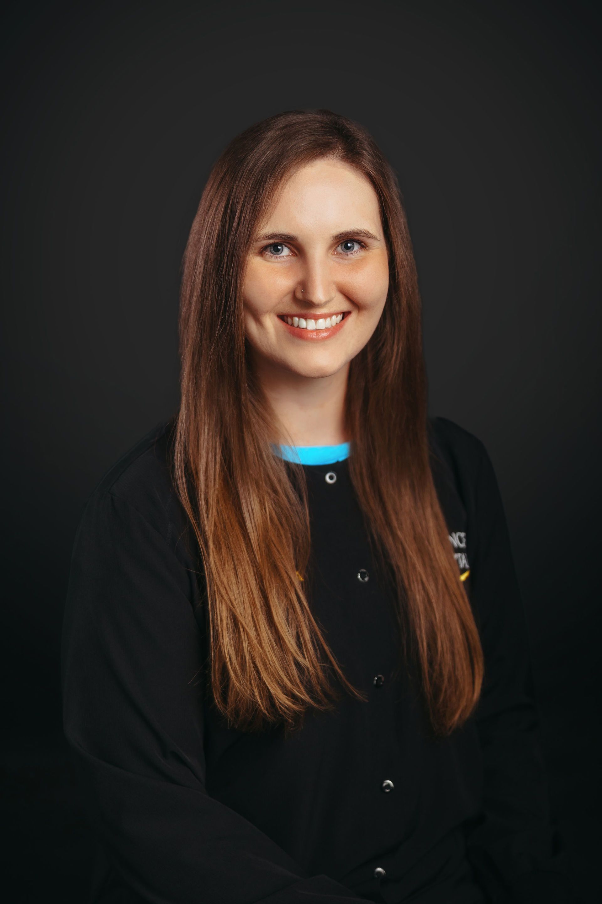 A woman with long hair is wearing a black jacket and smiling.