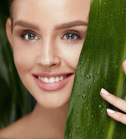 A woman is smiling while covering her face with a green leaf.