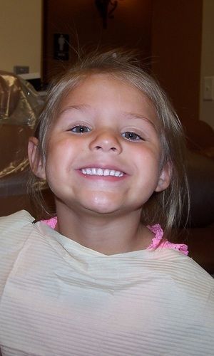 A little girl is smiling while sitting in a dental chair.