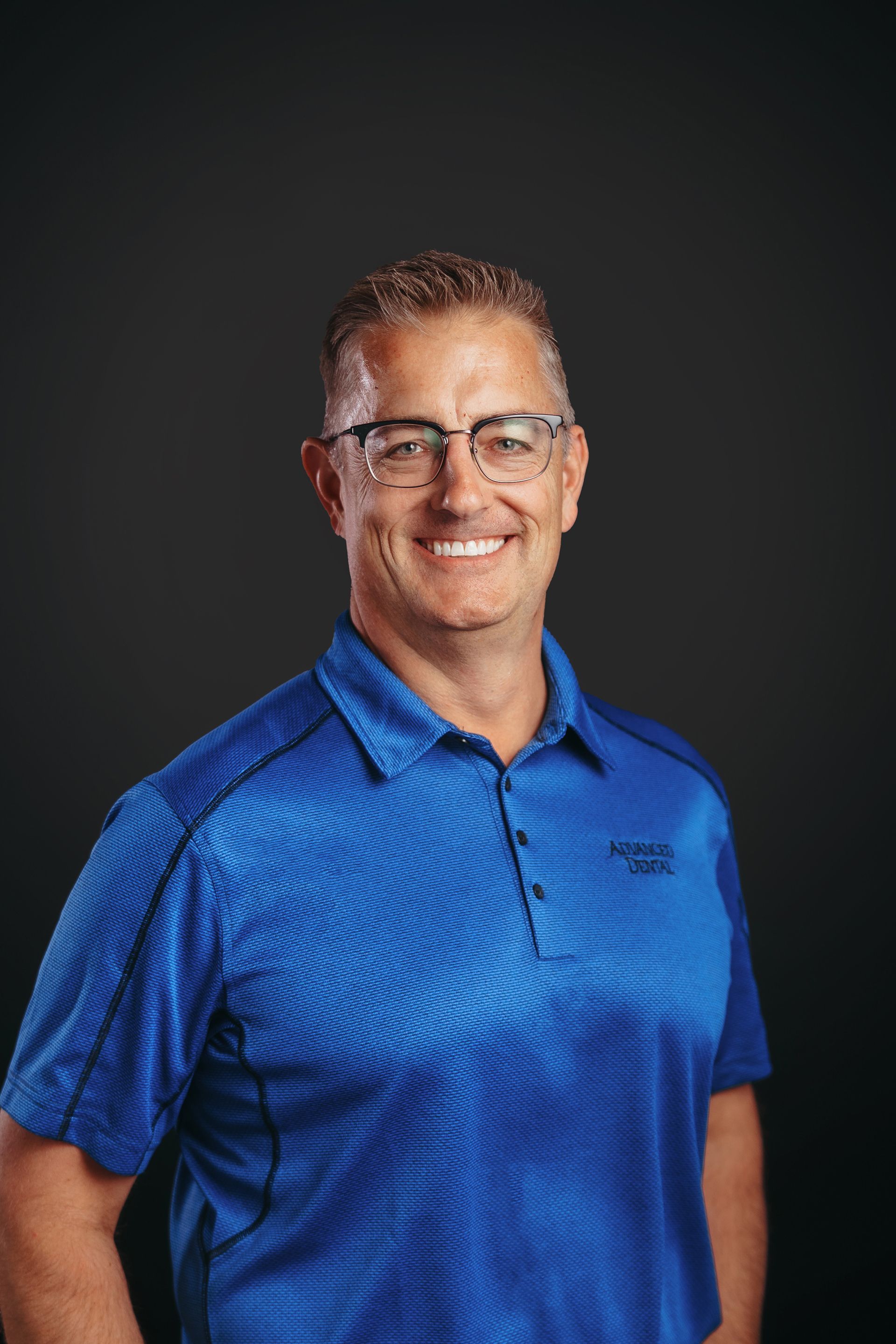 A man wearing glasses and a blue shirt is smiling for the camera.