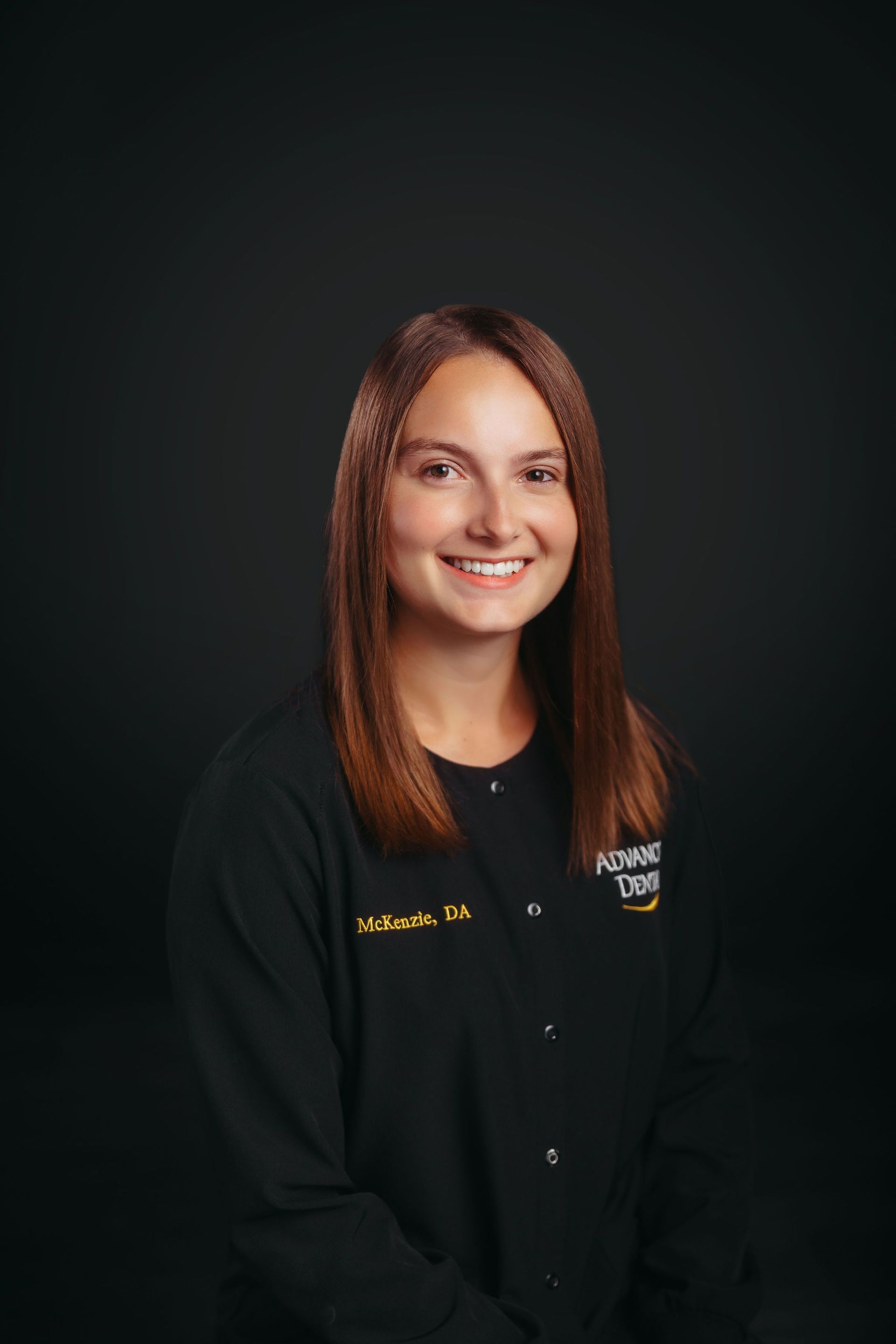 A woman in a black shirt is smiling in front of a black background.