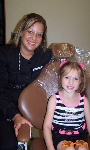 A woman is sitting next to a little girl in a dental chair.