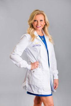 A woman in a white lab coat is standing with her hands on her hips.