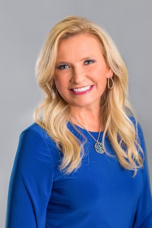 A woman in a blue shirt and necklace is smiling for the camera.