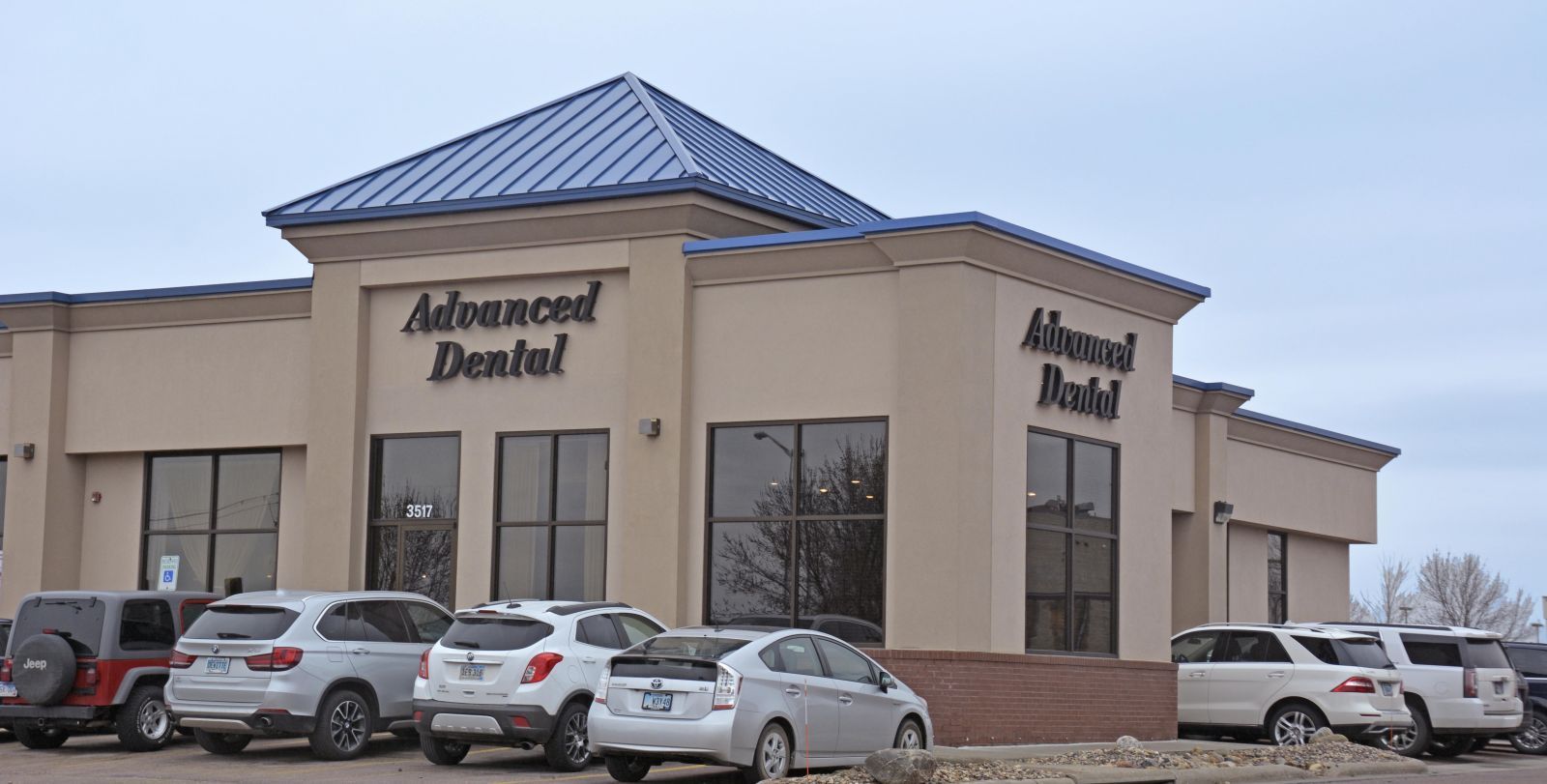 A row of cars are parked in front of an advanced dental office.