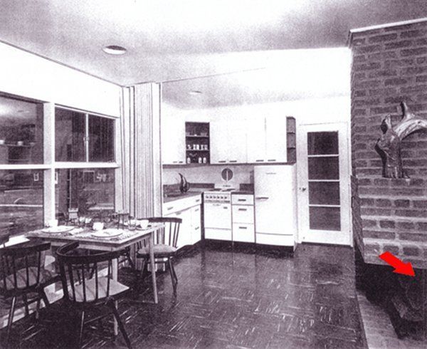 Kitchen-dining room with table, cabinets, brick wall, and a red arrow pointing to a chair
