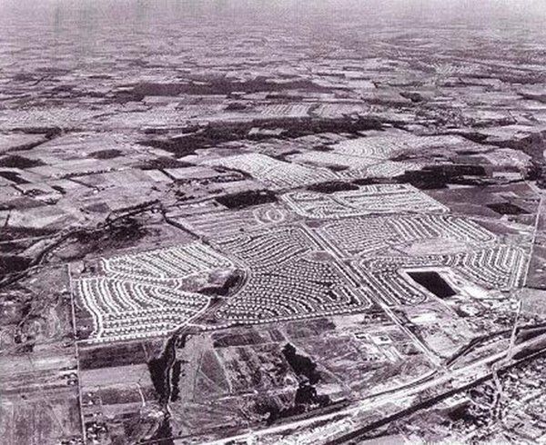 Aerial view of a sprawling suburban housing development with roads and fields in black and white.
