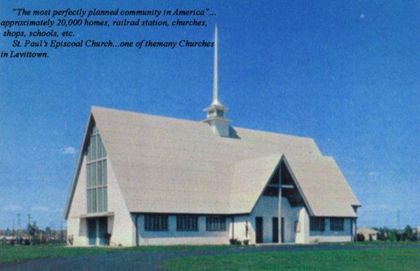 A white A-frame church with a steeple on a grassy field under a blue sky