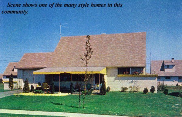 Suburban house with steep brown roof, white walls, and green lawn under a clear blue sky