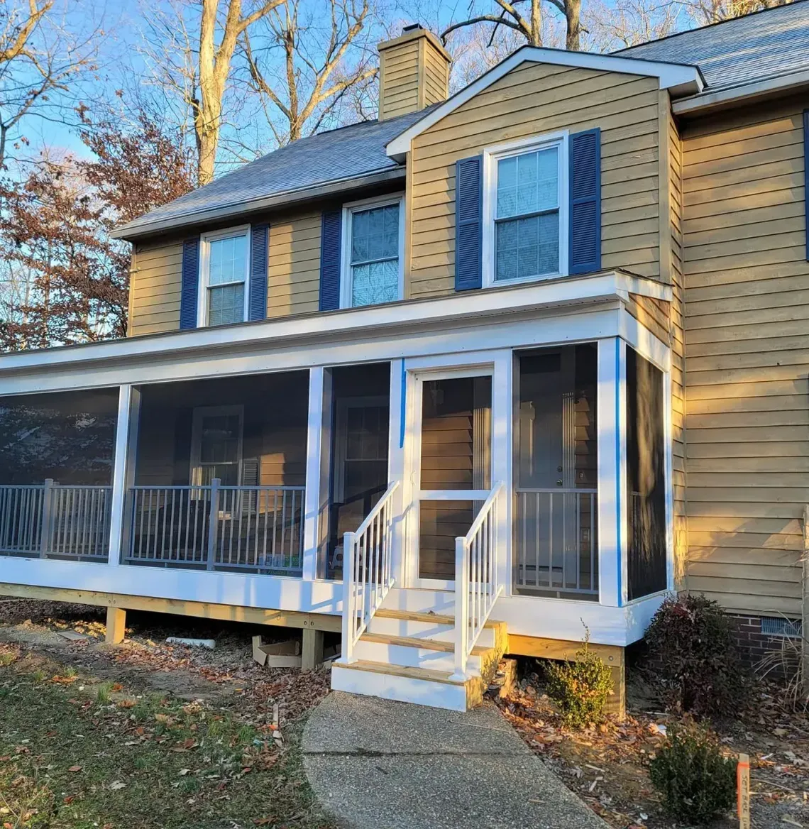 Yellow brick house with a screened-in front porch and white trim amid autumn trees