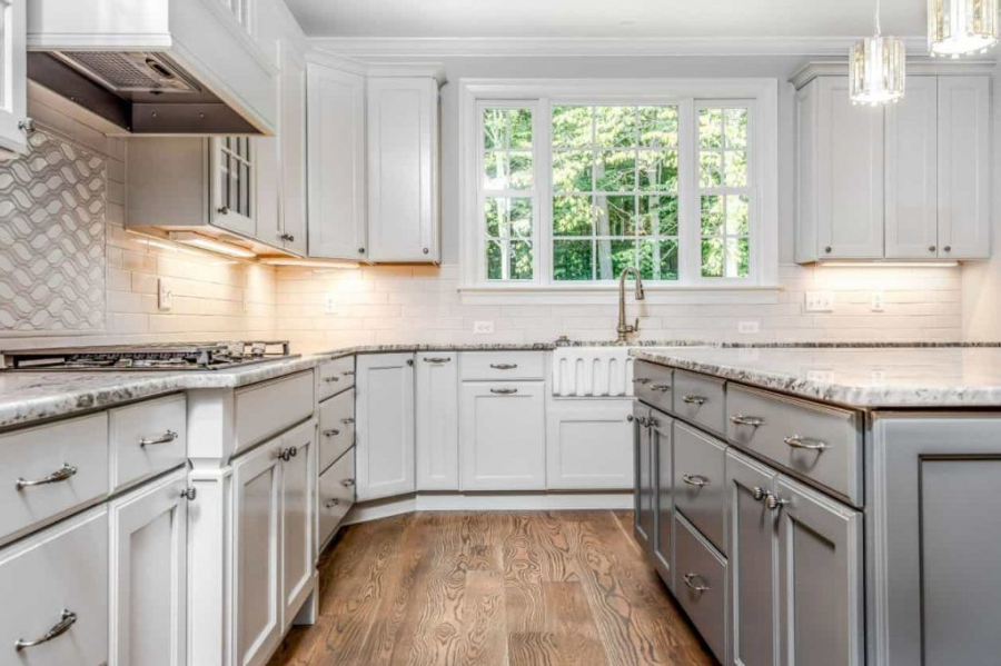 Bright white kitchen with marble countertops, stainless appliances, and a window over a farmhouse sink