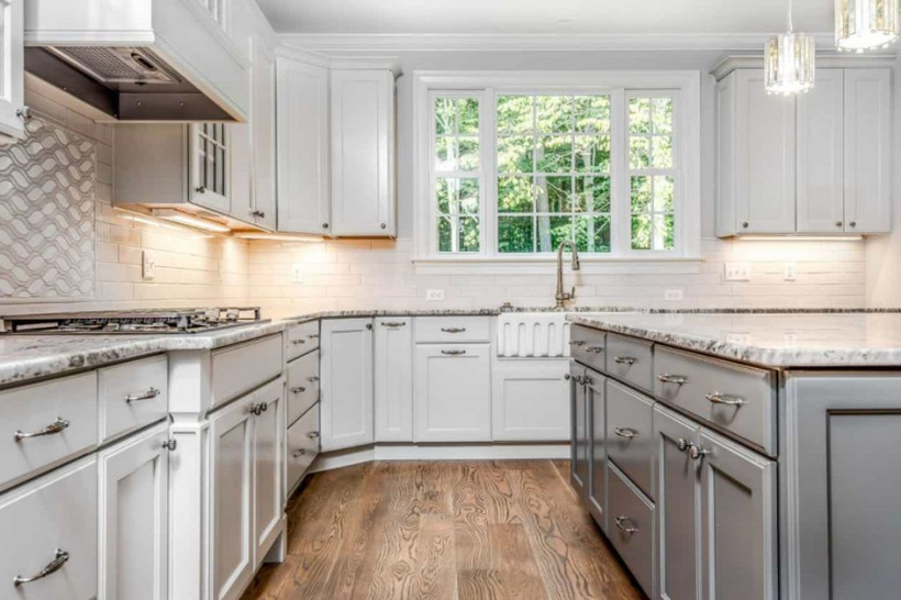 Bright white kitchen with marble countertops, stainless appliances, and a window over a farmhouse sink