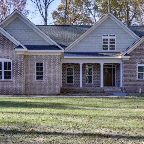 Brick suburban house with gray gabled roof, white trim, and front porch behind a grassy lawn
