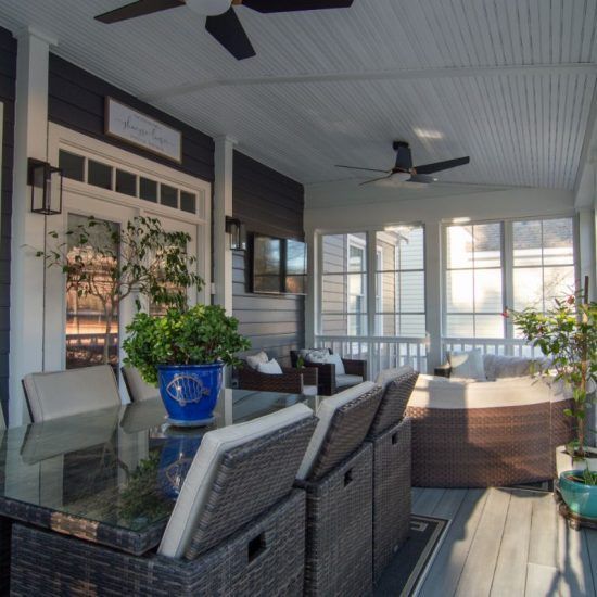 Covered porch with wicker dining set, blue potted plant, ceiling fans, and sunlight streaming through screens