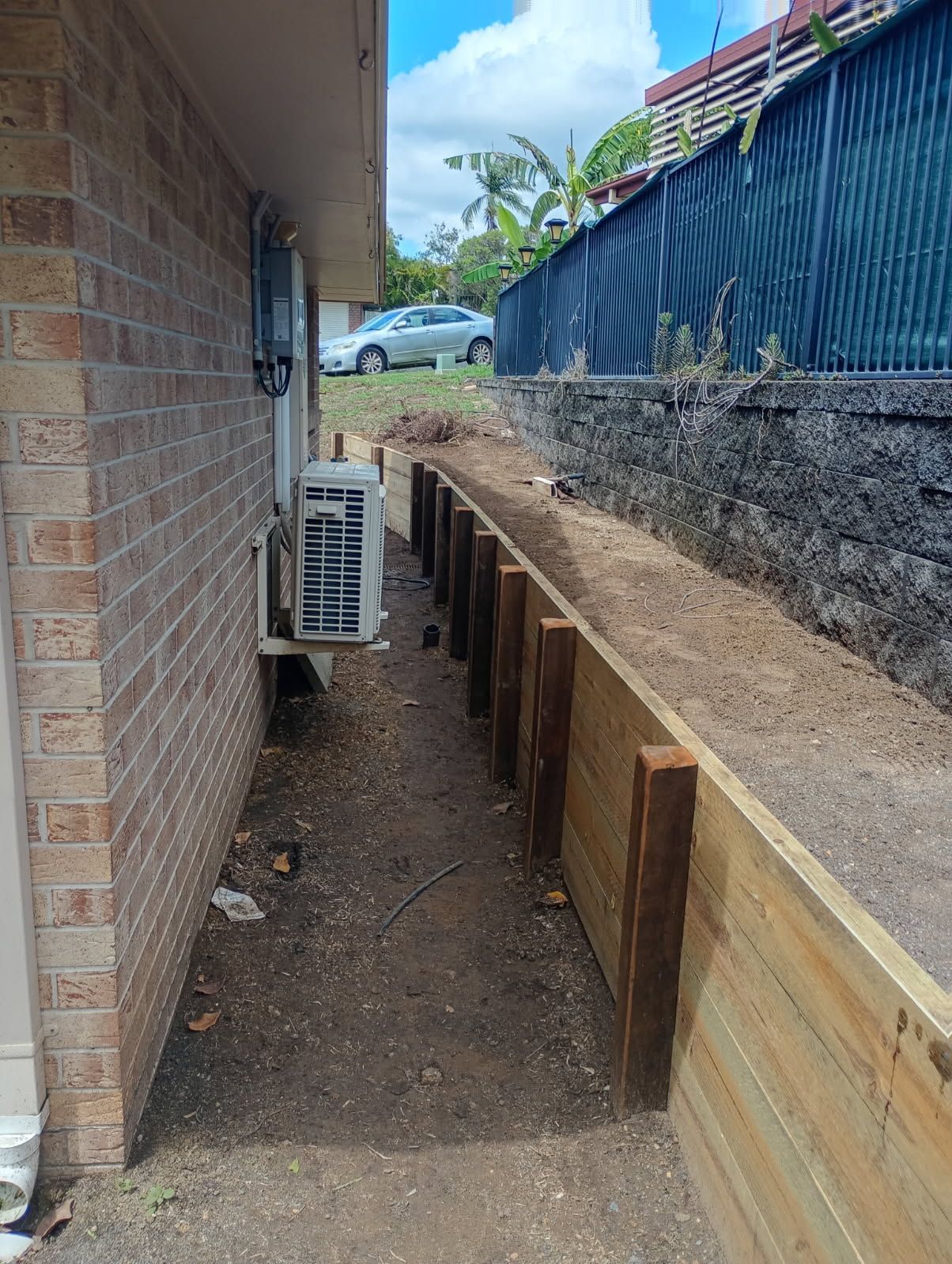 Narrow Dirt Walkway Between a Brick Building and a Wooden Retaining Wall — The Fence Place in Kawana, QLD