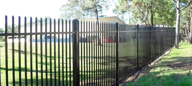 A black metal picket fence standing on a grassy lawn with trees in the background.