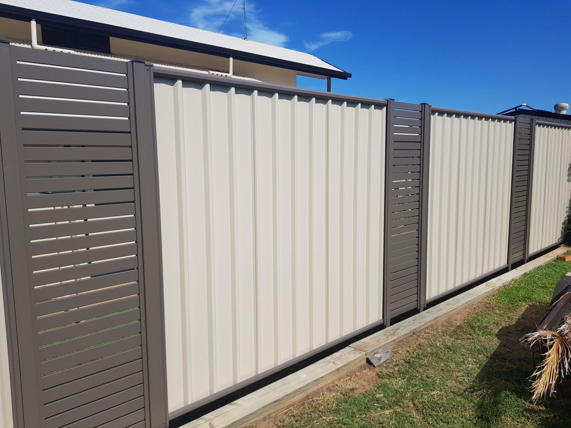 Beige metal fence with dark gray posts and a clear blue sky.