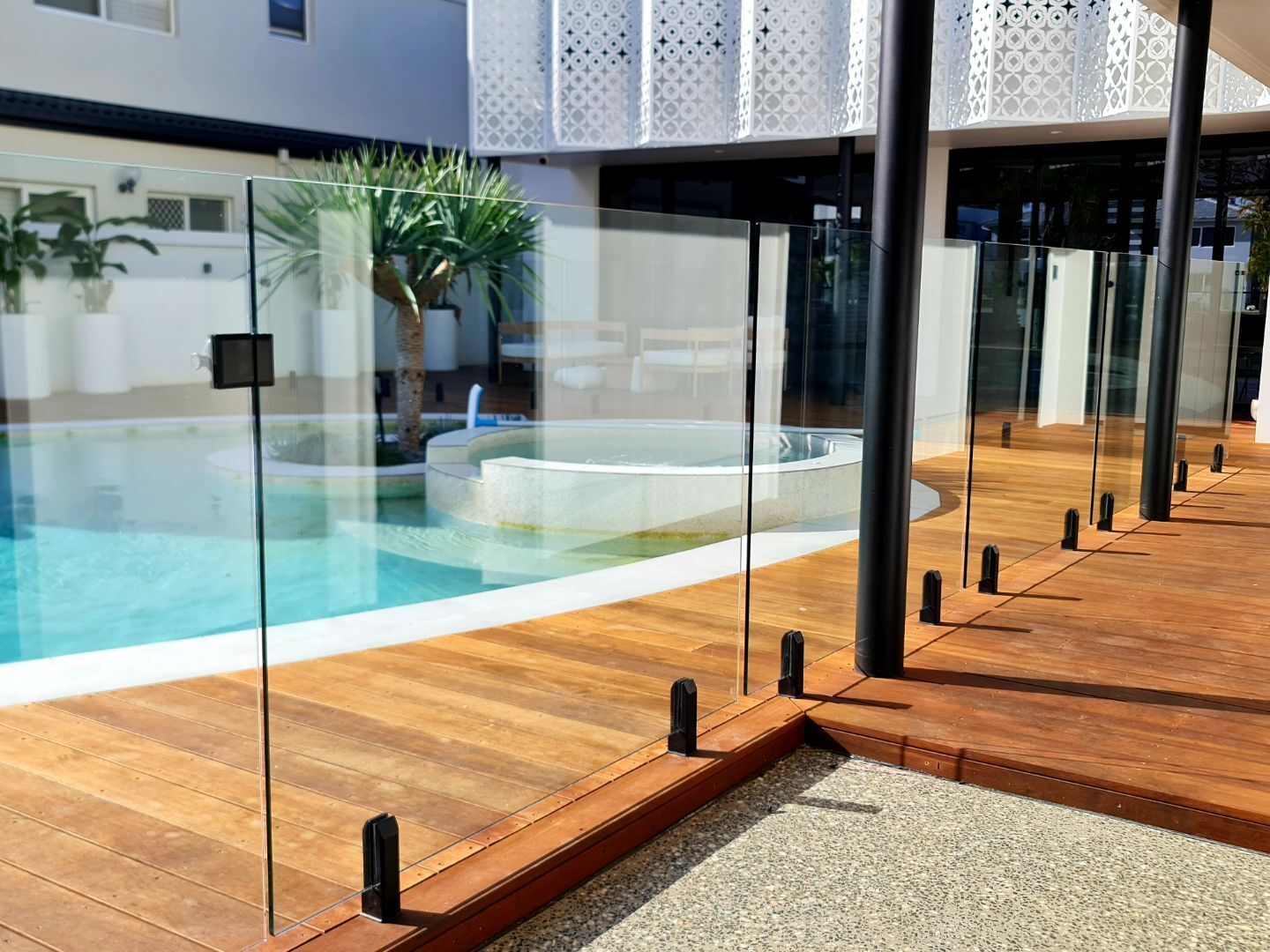 A frameless glass pool fence on a wooden deck next to a swimming pool and a modern building.