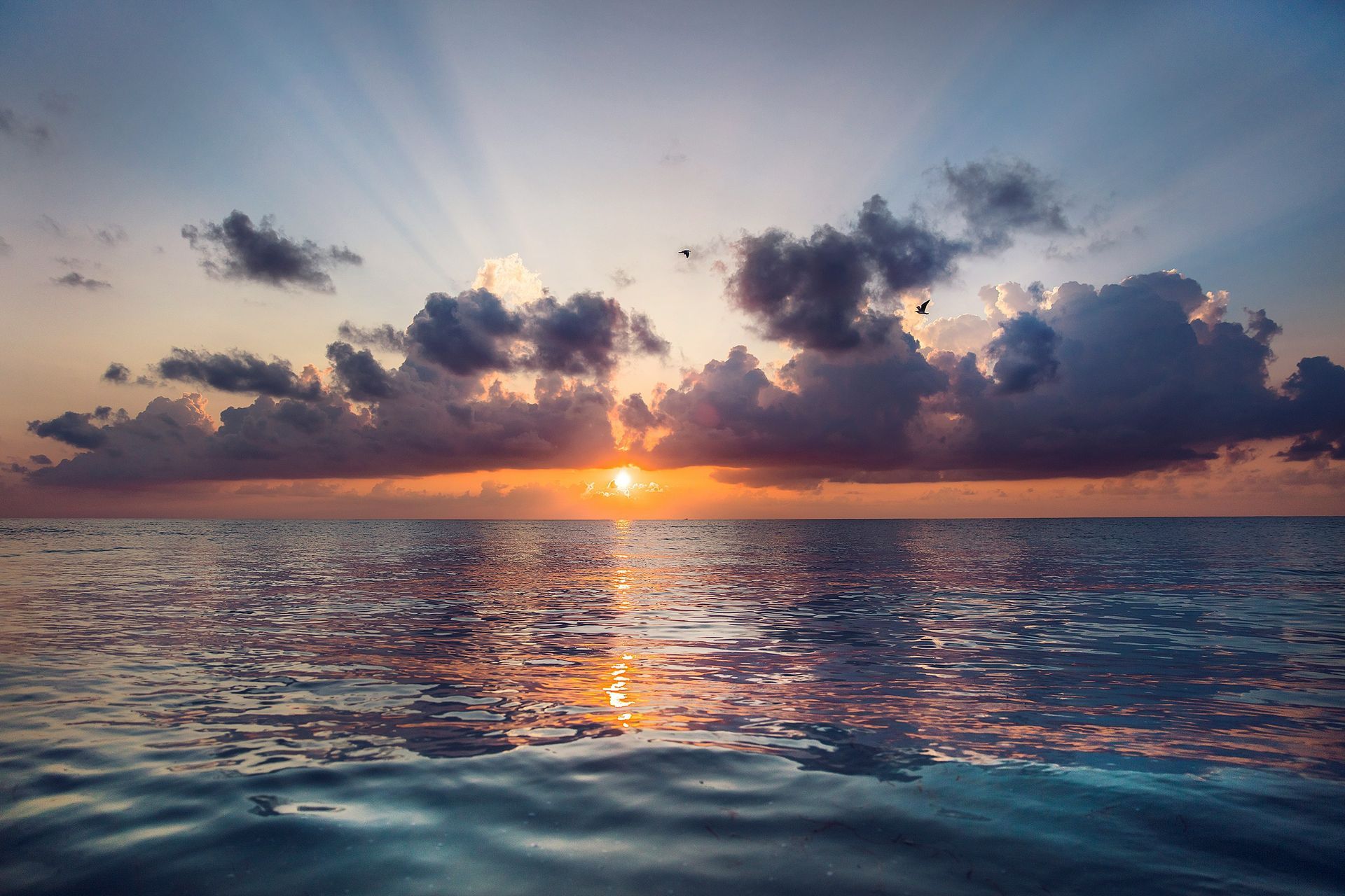 the sun is setting over the ocean with clouds in the sky