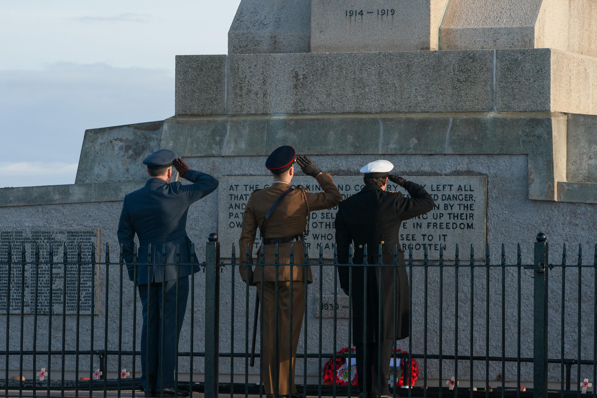 Three uniformed service members saluting a war memorial.