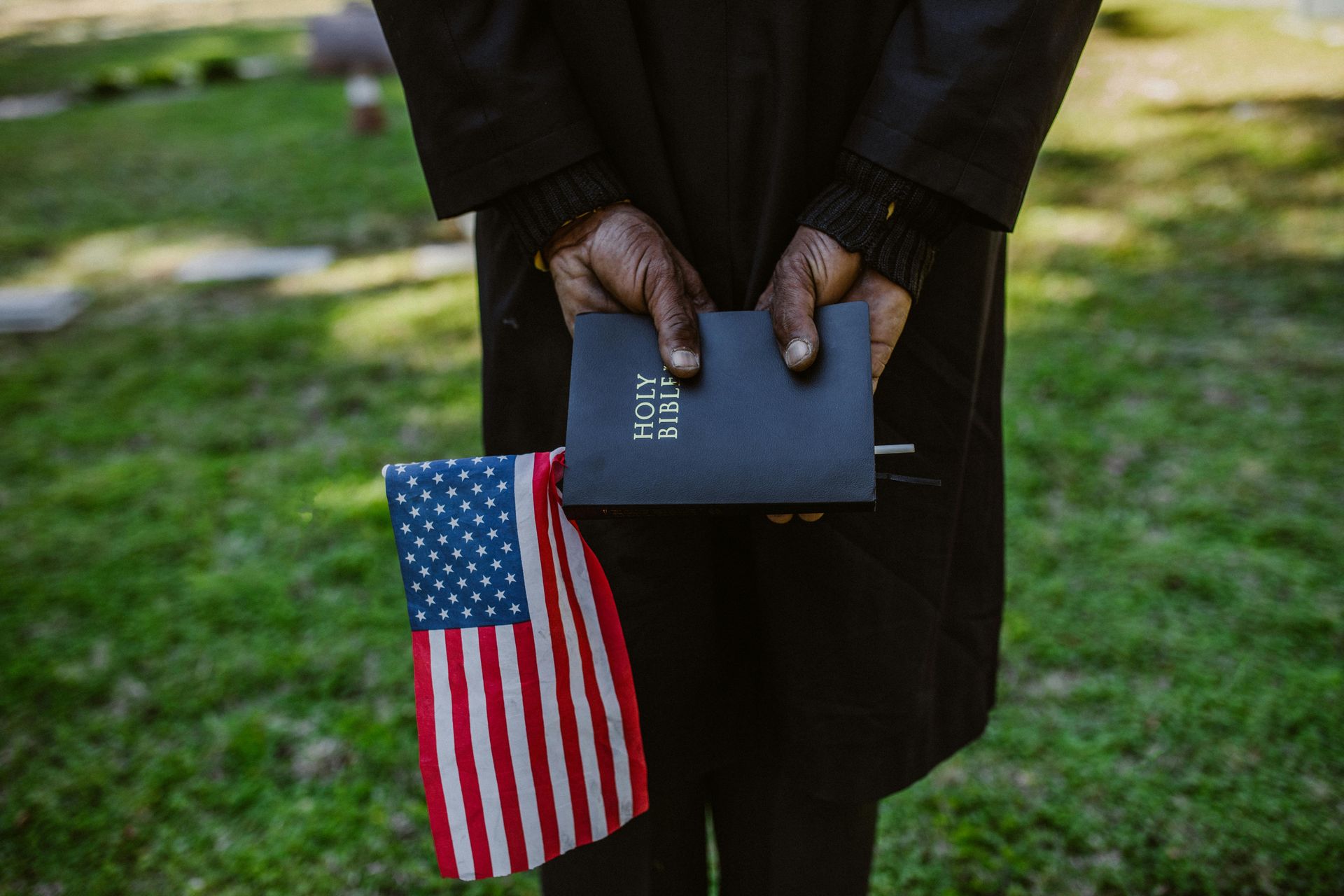 Person holding a Bible and American flag at a cemetery.