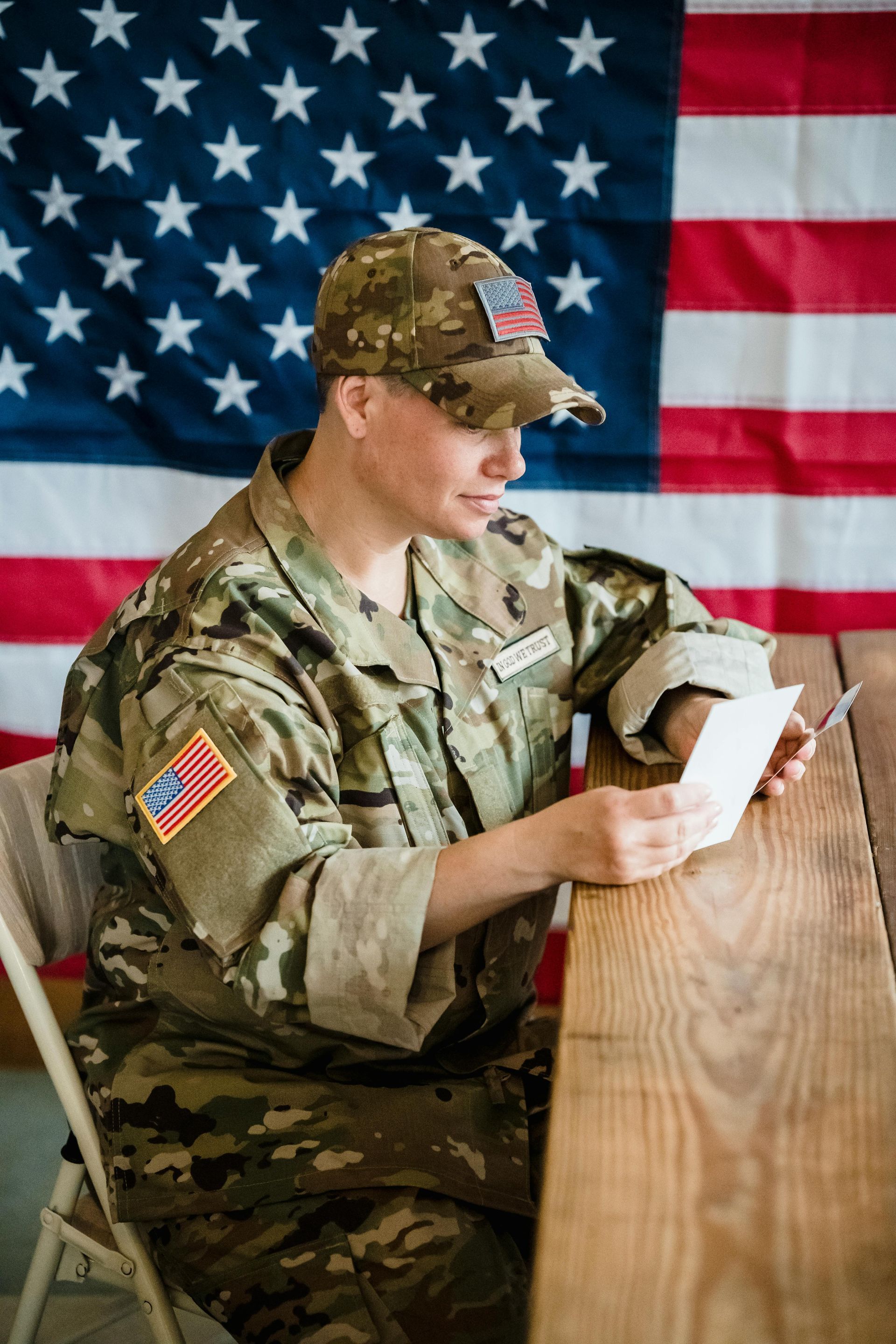 Soldier in camouflage reads a letter, American flag in background.