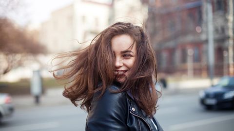 A woman in a leather jacket is smiling with her hair blowing in the wind.