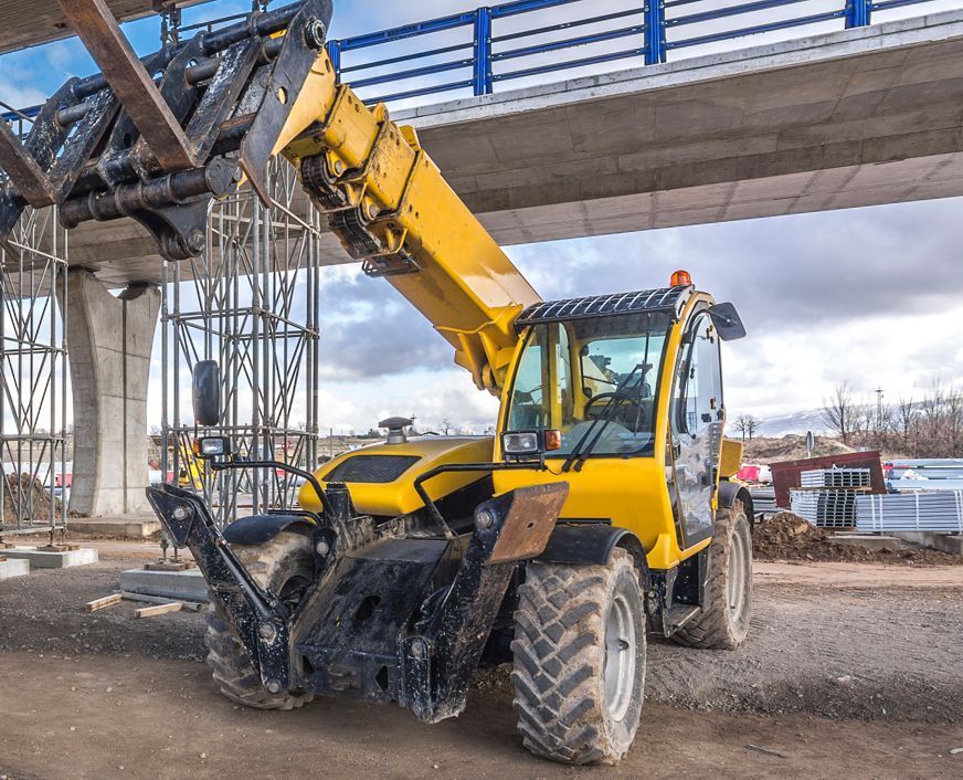 A yellow forklift is sitting under a bridge on a construction site.
