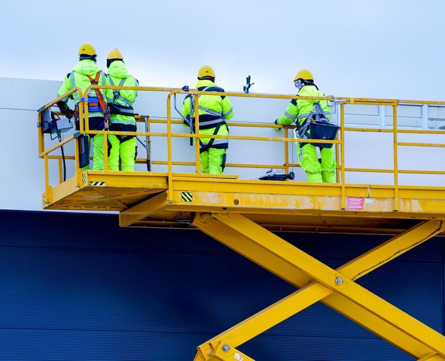 A group of construction workers are working on a yellow scissor lift.