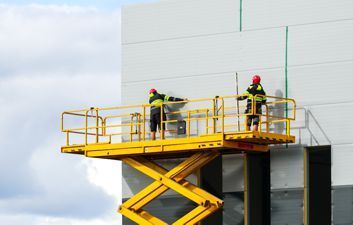 Two men are standing on a yellow scissor lift.