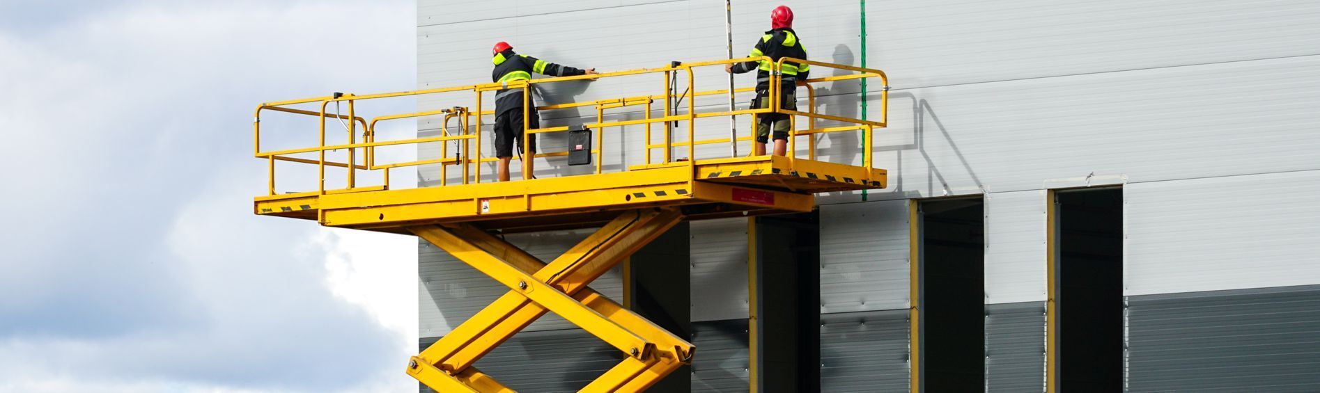 Two men are standing on a yellow scissor lift.