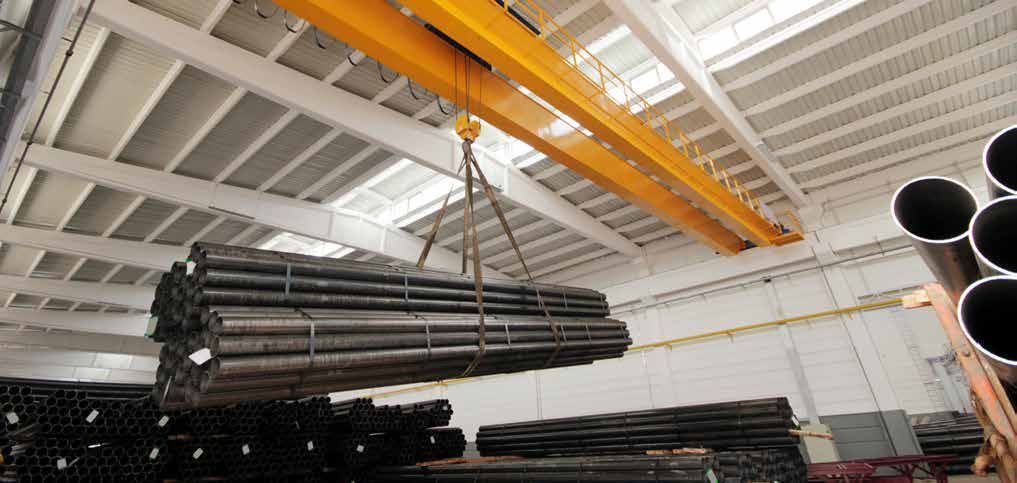A crane is lifting a stack of pipes in a warehouse.