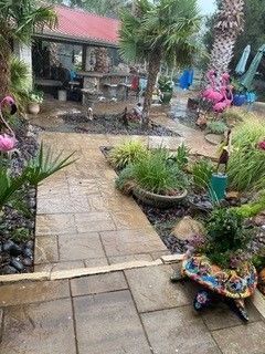 A stone patio leads to an outdoor bar under a red roof, surrounded by tropical plants and decorative flamingo statues.