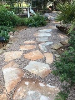 A winding garden path made of large, flat tan stepping stones set into a bed of small gray gravel.