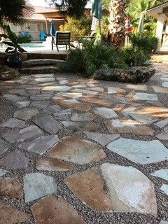 A stone patio made of irregular tan and gray flagstones with gravel between them, leading to steps and a backyard pool.