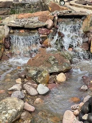 A small, tiered stone waterfall flowing into a rocky stream.