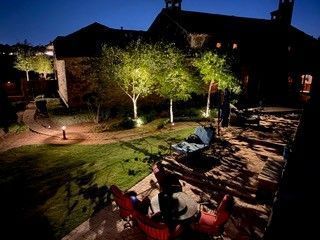A house patio at night with illuminated trees, garden lighting, and outdoor seating furniture.