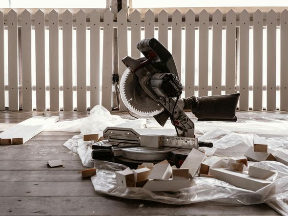 Mitre saw on a plastic sheet, surrounded by cut wood scraps; white picket fence in background.