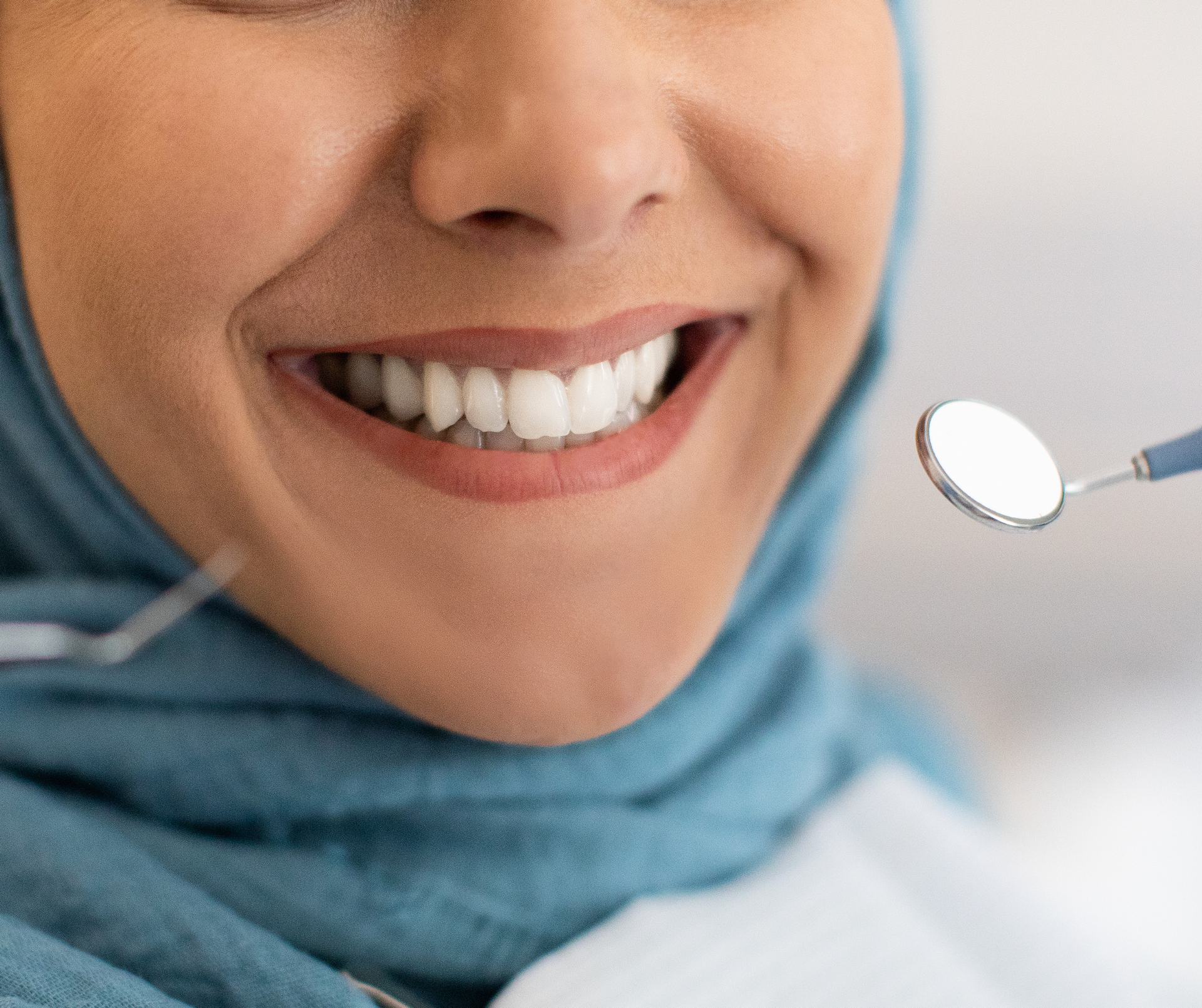 Woman smiling, at dentist. Light blue hijab, dental instruments in view.