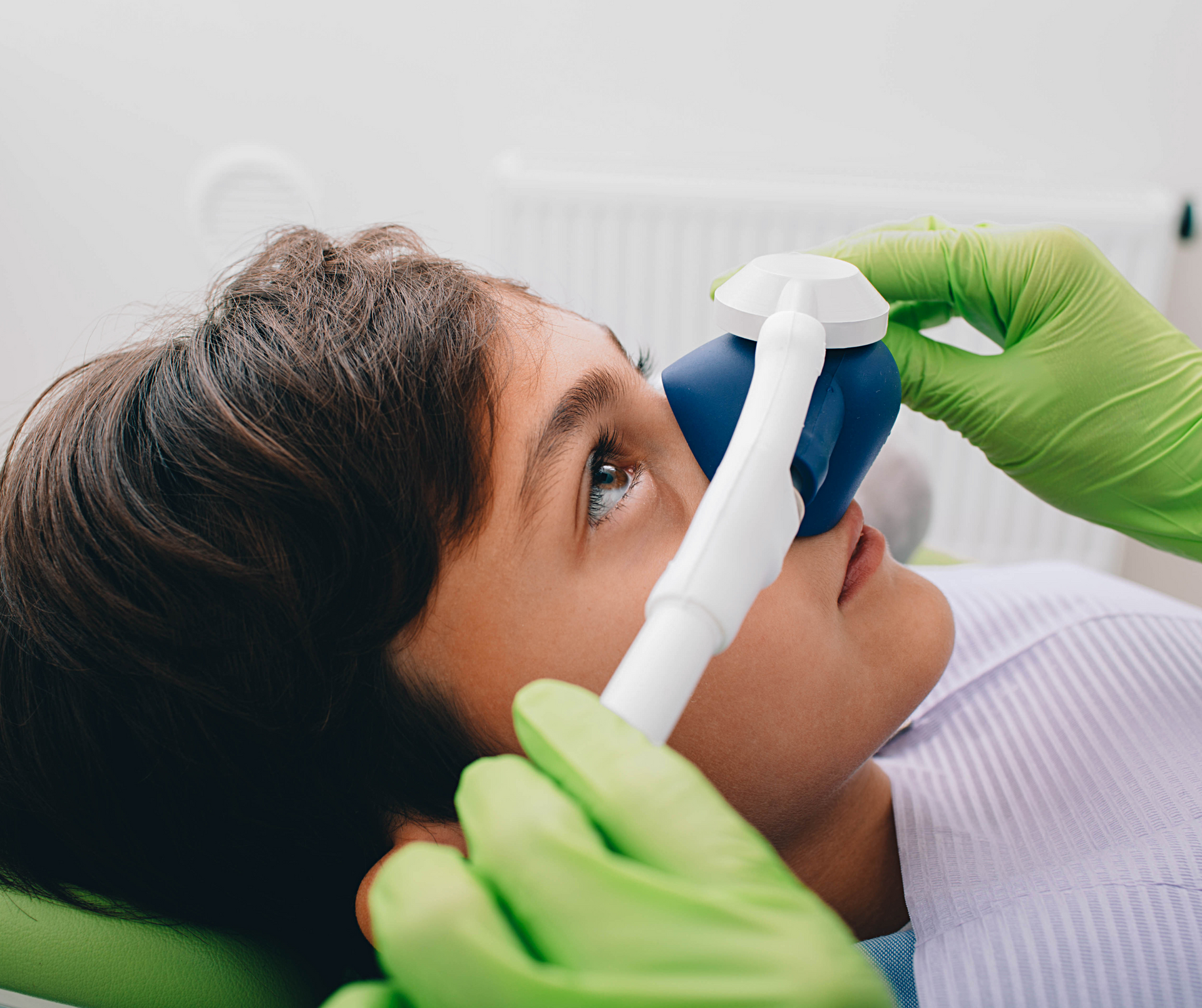 Young person receiving dental sedation via mask, eyes open, in dentist's office. Green gloved hands.