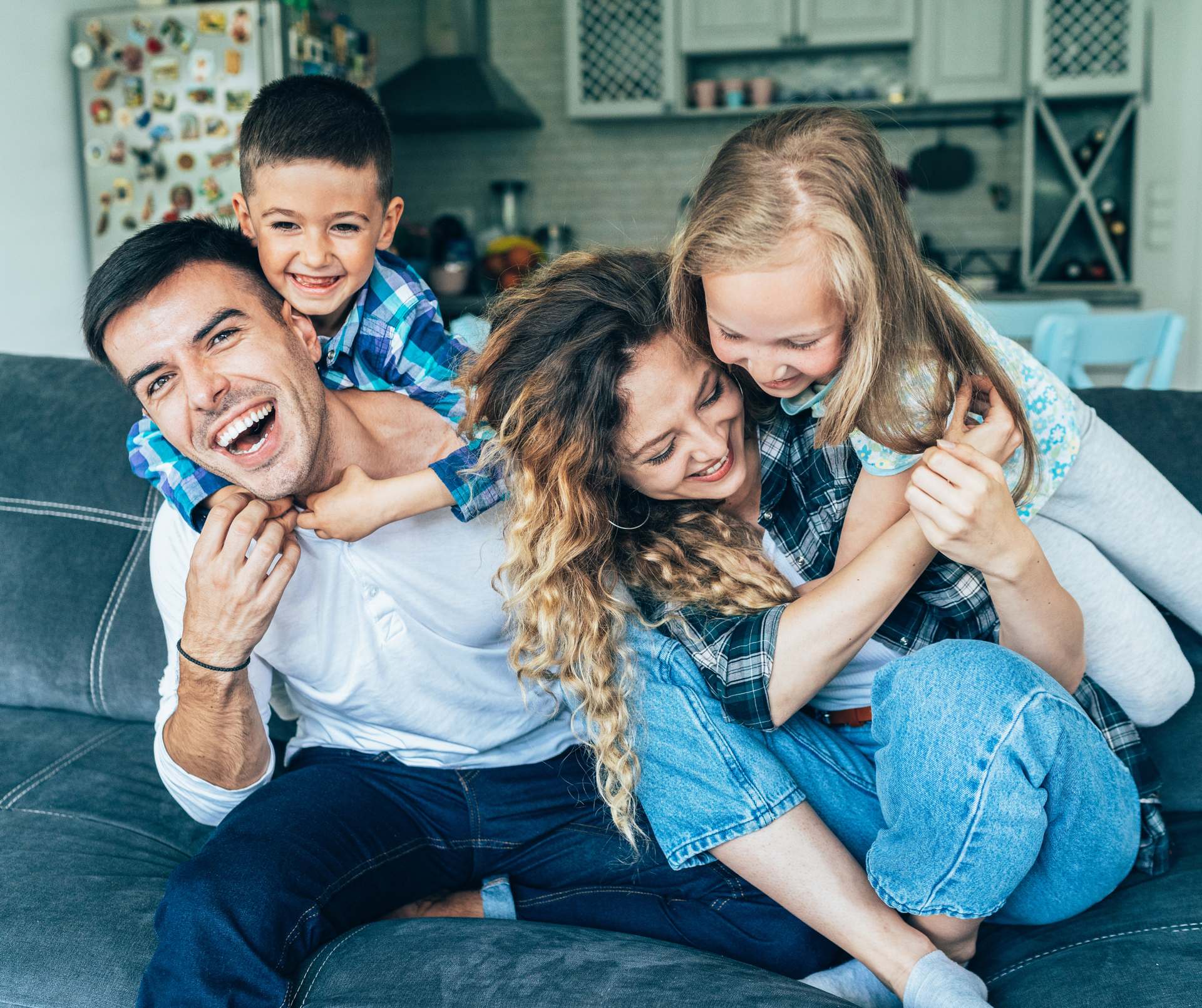 Family of four playfully embracing on a sofa, smiling.